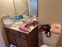 Makeup and personal care items arranged on a bathroom countertop and toilet tank, including nail polishes, cosmetic bags, and other travel accessories.