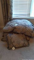 Close-up photo of two large decorative pillows with brown-beige damask floral pattern and ruffled trim