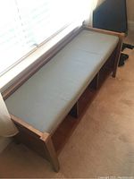 Full view of the wooden window bench with light gray cushion, showing the overall shape and structure.