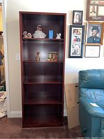 Full front view of the tall, dark wooden bookshelf with five shelves, placed against a wall with some decorative items on it.