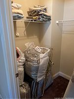 Closet with queen comforters, some in protective bags and others stacked on shelves and floor