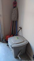 Full view of gardening hose reel box, mop, broom, shovel, and snow shovel leaning against wall