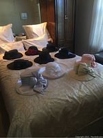 Overview of ten ladies hats arranged on bed, various colors and styles visible