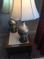 Side view of two matching table lamps on a wooden side table with beige floral painted glass bases and white fabric shades.