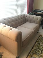 Front and side view of beige loveseat showing tufted back and arms, two seat cushions, and fabric upholstery.