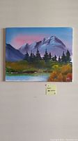 Full view of the canvas painting showing a mountain landscape with trees and a reflective lake under a pastel sky.