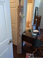 Rolled up beige patterned area rug leaning against door with adjoining desk and chair visible in background.