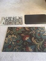 Three rugs arranged on a light carpet. Largest is floral fabric with rubber backing. Smaller are kitchen text design and plain brown rubber.