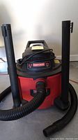 Front view of Craftsman wet/dry vacuum showing the red and black vacuum with hose and two black vertical extension wands attached on sides