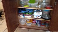 Open kitchen cabinet showing top and bottom shelves filled with various storage containers including Copper Chef bowls, salad spinners, Tupperware bowls, and lids.