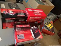 Overview of three boxed Motomaster air compressors and two boxed Noma power bars on table.