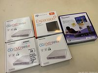 Lot overview showing all five boxed items: three Memorex CD/DVD writers, Seagate Expansion 8TB external hard drive, and HomeWorx ATSC digital converter box.