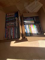 Photo of two open cardboard boxes filled with DVDs and Blu Rays arranged vertically, containing a mix of movies, TV shows, and documentaries.