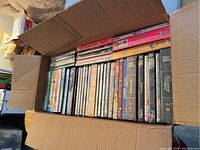 Open cardboard box filled with assorted DVDs showing spines and titles, including The Lord of the Rings and others.