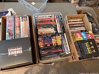 Three bins and cardboard boxes full of DVD cases arranged on a table