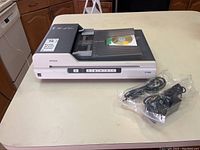 Epson GT-1500 flatbed scanner with power and USB cable on table in closed position with compact disc on feeder.
