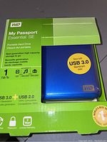 Packaged WD My Passport Essential SE portable hard drive, blue, shows 1 TB capacity and USB 3.0/2.0 interface