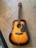 Full view of the sunburst finished 6-string acoustic guitar laid flat on carpet.