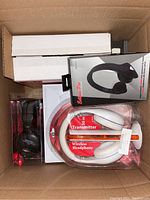 Top view showing several electronics and headphone boxes in a cardboard box, including Kross wireless headphones, studio style headphones, and white wireless headphones with transmitter.