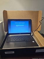 Open laptop in shipping box showing keyboard and display with Windows language selection screen