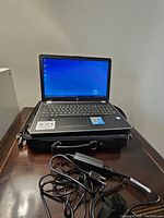 Laptop powered on resting on black laptop bag with charger and cords in front