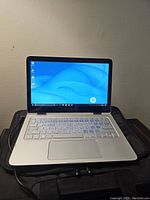 Laptop open on top of black bag showing display, keyboard and power cable connected