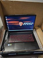 Open laptop in shipping box showing screen, keyboard and power cable