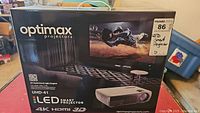 Front of sealed retail box showing Optimax LED Smart Projector branding and label