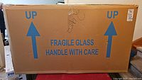 Closed cardboard carton marked “Fragile Glass Handle With Care” and UP arrows.