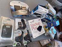 Photo showing various packaged electronic items including Seagate Backup Plus external drive, frozen in plastic packaging digital clocks, Grundig Mini 400 radio, and other small electronic accessories.