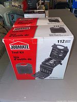 Photo showing unopened box of Jobmate 112-piece tool kit, depicting carrying case with handle and example layout of tools inside.