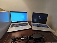 Two open HP EliteBook laptops side by side with power adapter in foreground