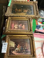 Three framed vintage art pieces arranged on a flat surface showing ornate gold frames and varied indoor scenes, one canvas with damage.
