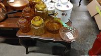 Photo of five amber glass canisters, two amber glass bowls, and one clear vintage glass bowl on a wooden table.