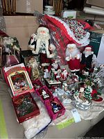 Wide view of multiple Christmas items including Santa figurines, bird ornaments, and tablecloths arranged on a seat.