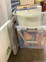 Two plastic bins containing various board games and puzzles stacked inside storage containers, showing box edges and sides.