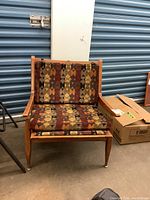 Wood framed chair with removable cushions in geometric patterned fabric in shades of rust, brown, black, orange, beige. Chair with scratches and wear.