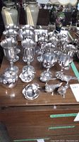 Lot of pewter and silverplate goblets, bird salt and pepper shakers, apple bowls, and chrome apple trinket box on wooden surface.