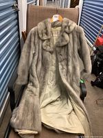 Full view of the long mink coat open on chair to show sleeves, collar, and fur texture.