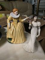 Two Franklin porcelain statues, "Charlotte - The Quadrille" and "Katharine - The Calliard," shown together on shelf with background of boxes.