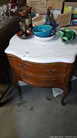 Full view of wooden side table with white marble top, adorned with miscellaneous decorative items (not included). Shows front curved design and drawer handles.
