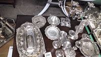 Wide view of the lot showing large silverplate 5-head candelabra, various candlesticks, trays, butter dish, and perforated cup with tray from West Germany all arranged on a table with visible inventory tags.