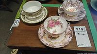 Four teacups and saucers grouped on wooden surface displaying various floral designs and gold trims.