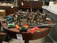 Wide view of vintage plastic soldier figures in olive green and blue with multiple vintage toy vehicles on a wooden round table, showing general lot content and condition.