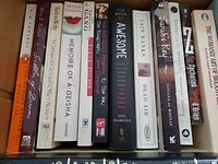 Spine view of the book lot showing titles including Memoirs of a Geisha, The Book of Awesome, Sarah's Key, and The Womanly Art of Breastfeeding.