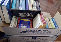Photo showing a box filled with multiple paperback and hardcover books stacked vertically and horizontally, titles include Debbie Macomber's Dakota Home.
