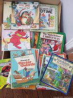 Box containing a visible selection of children’s story books including Merry Christmas Mom and Dad, First Book for Bedtime, Clifford, The Night Before Christmas, Travels of Doctor Dolittle, and Franklin's Blanket.