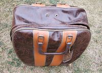 Closed view of the brown vintage leather bowling ball carrying bag with tan straps and small chain tag