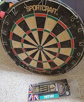 Photo of the Sportcraft dartboard and the boxed set of three threaded brass darts placed on carpet.