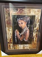 Photo of a large framed painting showing a detailed portrait of a woman with white shell jewelry and a headwrap, surrounded by tribal pattern borders.